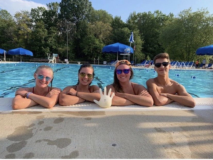 Junior Olivia Grindal, sophomore Alexis Fitzgerald, alumni Jacquee Clabeaux, and sophomore Ryan Brown pose with Boo the glove near the pool. The lovable mascot has been part of several Greenbriar pool trips and adventures throughout the summer. 