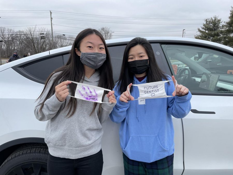 Seniors Lindsey Lim and Kristen Yoo hold up masks they decorated and brought to the Don’t Stop Believin’ Tailgate event in March.