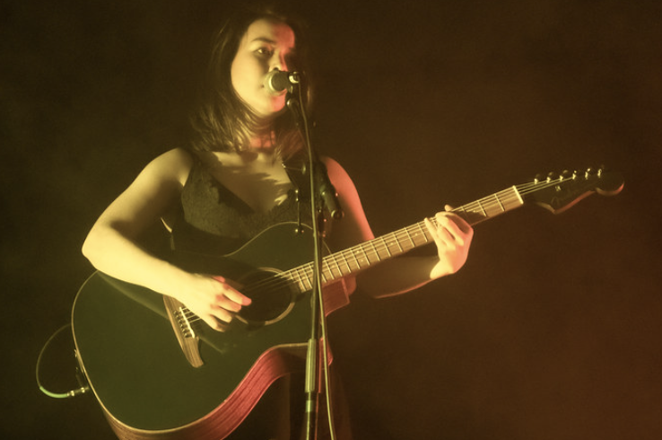 Mitski plays guitar and sings at a concert by, licensed under CC BY-SA 2.0 
