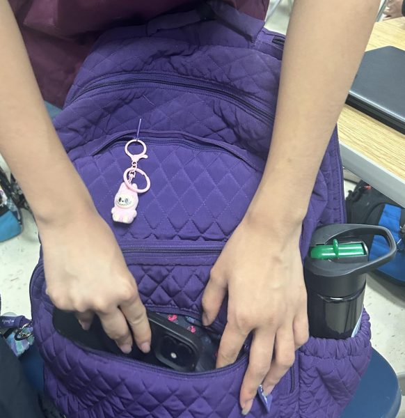 A student puts their phone in their bag before the 8:10 bell rings to comply with the phone policy.