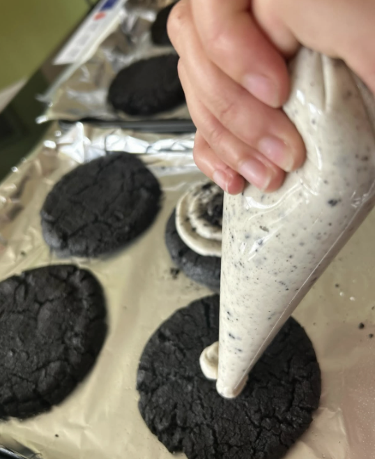 Junior Julia Pollard pipes cookies and cream frosting onto freshly baked chocolate cookies on July 25.
Photo used with permission of Julia Pollard