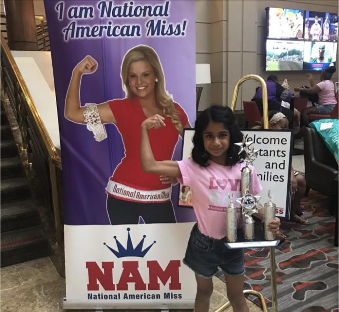 I pose in front of the National American Miss banner at my very first pageant in 2018 after winning the talent optional competition. Photo used with the permission of Kirti Patel. 

